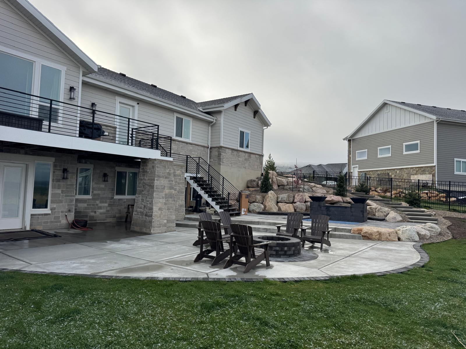 Wide angle view of backyard fire pit paver patio with manicured lawn and mature trees, Northern Utah