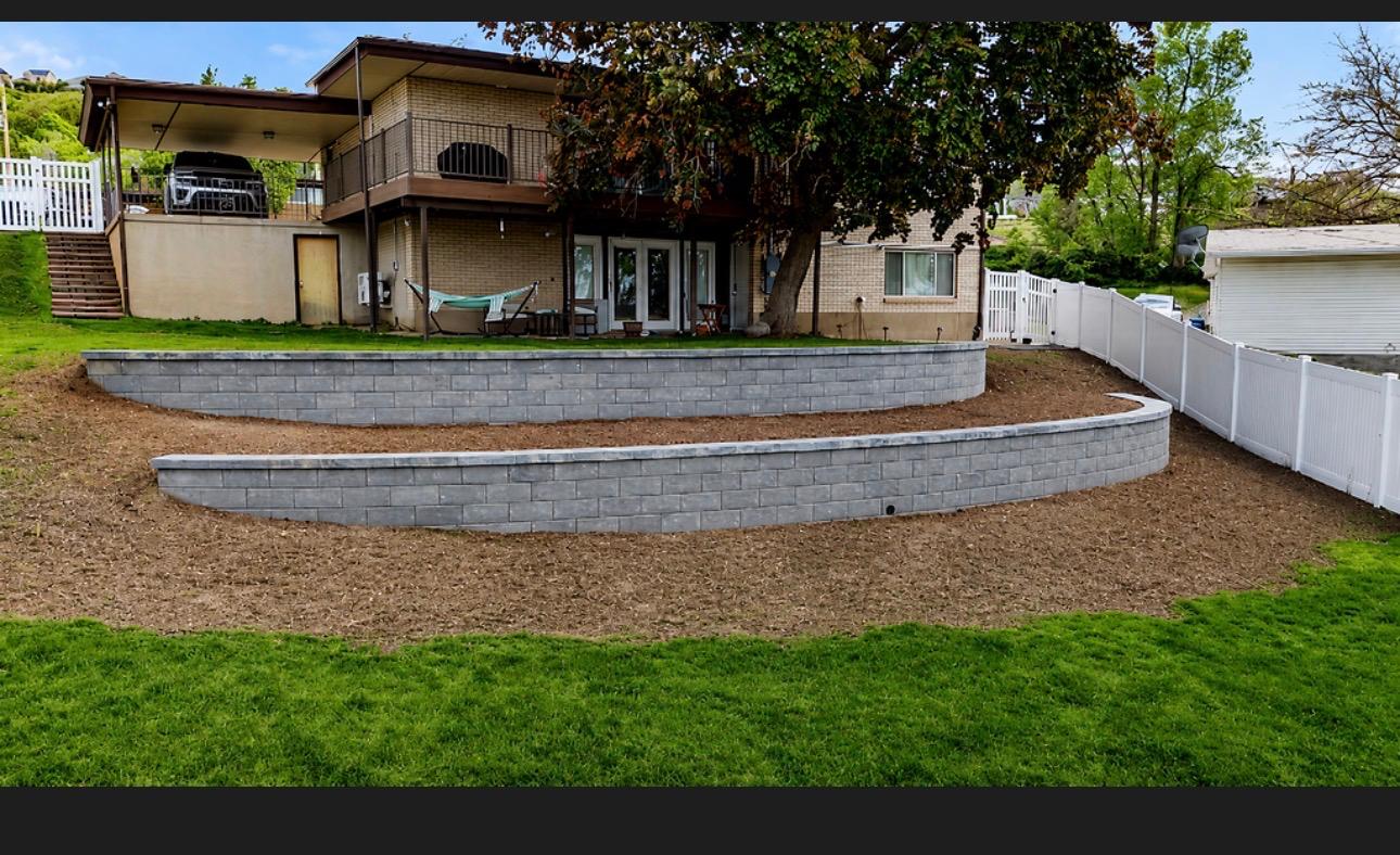 Curved natural stone retaining wall creating level lawn area in sloped backyard, Northern Utah landscaping